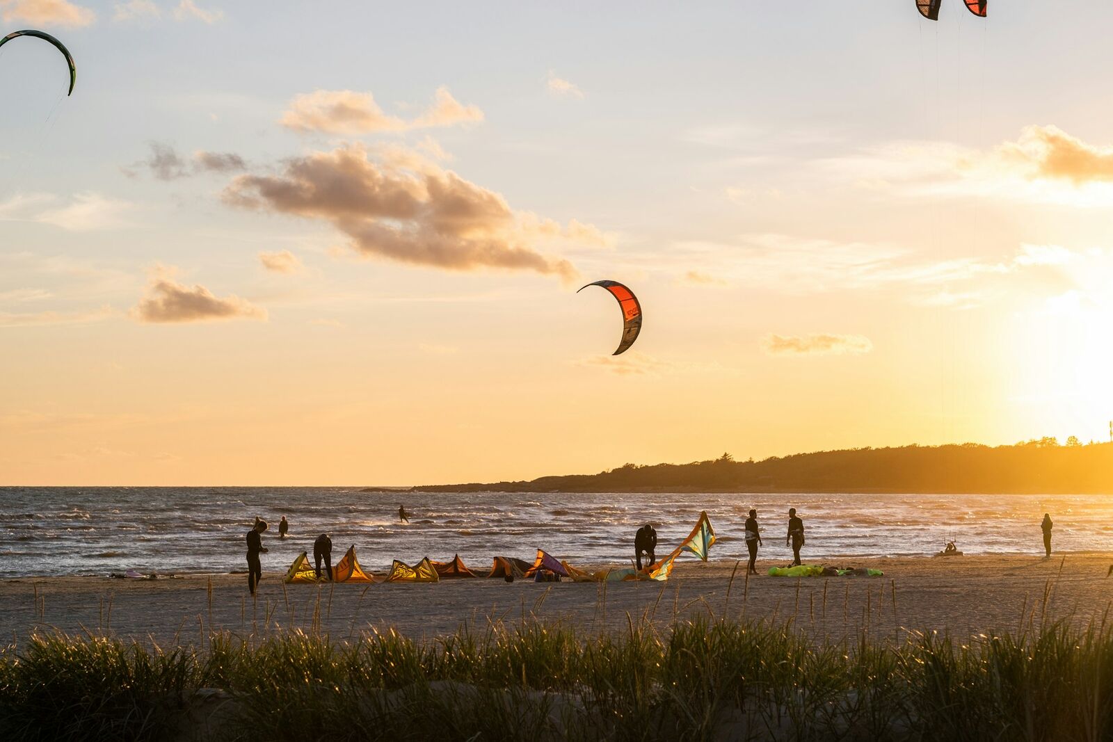 Kitesurfing kites laid out on a beach at sunset while riders pack up their gear