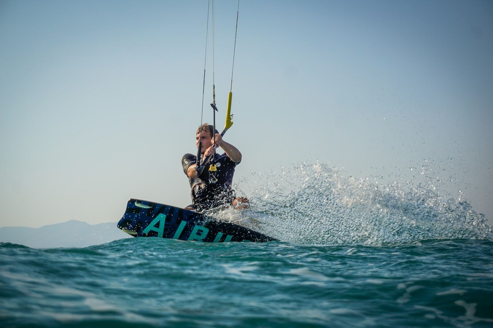 Kitesurfer carving a turn across flat water with spray kicking up behind the board