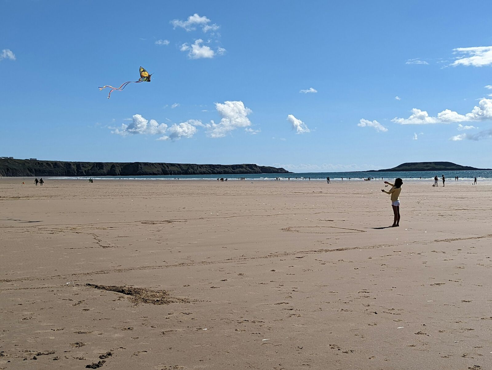 Wide, sandy kitesurfing beach with turquoise water and distant kites